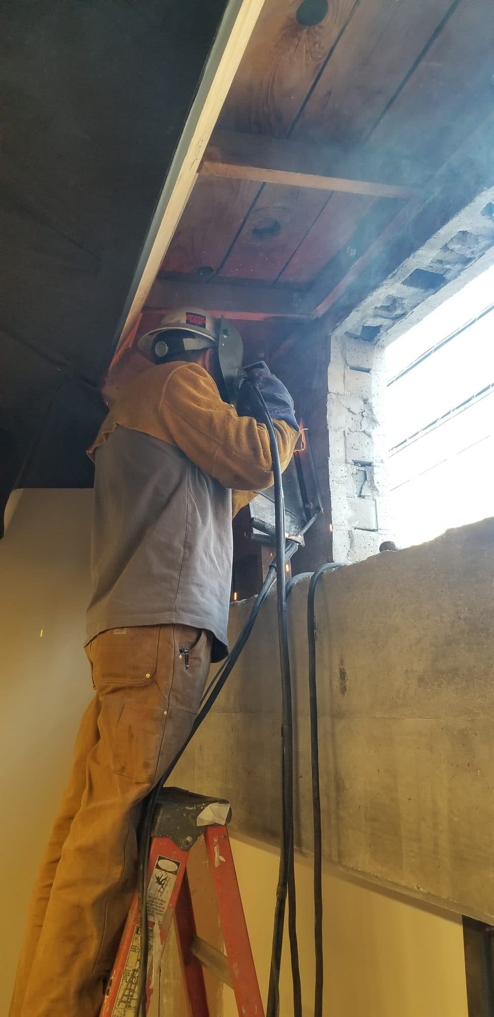 Welder in full PPE welding steel at a new window opening